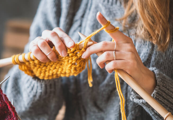 Close up of women knitting with yellow yarn.